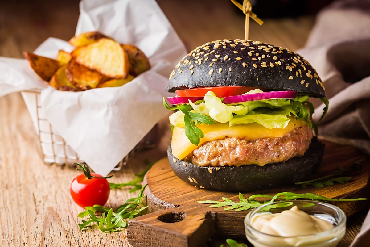 A gourmet burger with a black bun and fresh toppings on a wooden board.