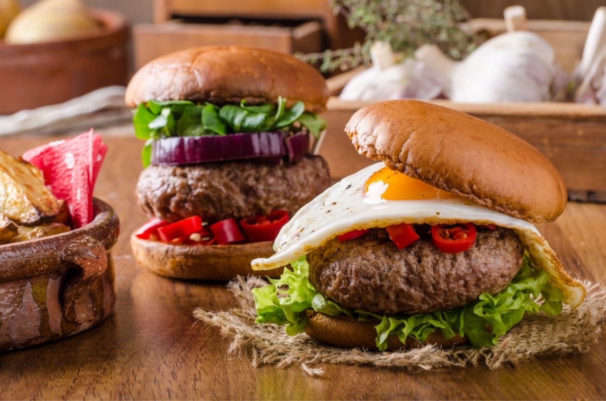 Two juicy burgers with fresh vegetables and cheese on a wooden surface.