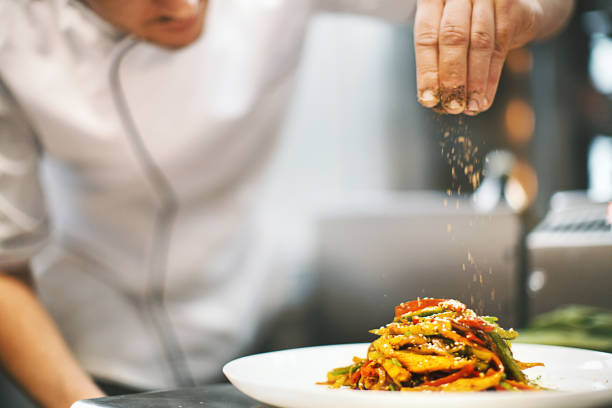 Chef sprinkling seasoning over a plated pasta dish.