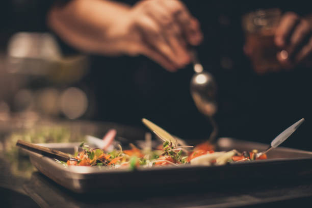 Chef garnishing a dish with fresh herbs in a kitchen.